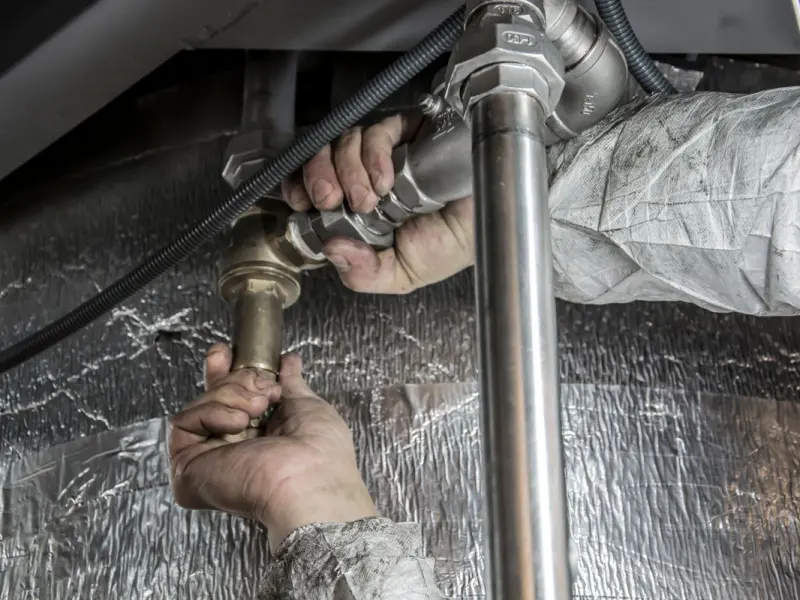 Plumber tightening a steel supply pipe fitting with a wrench under a sink