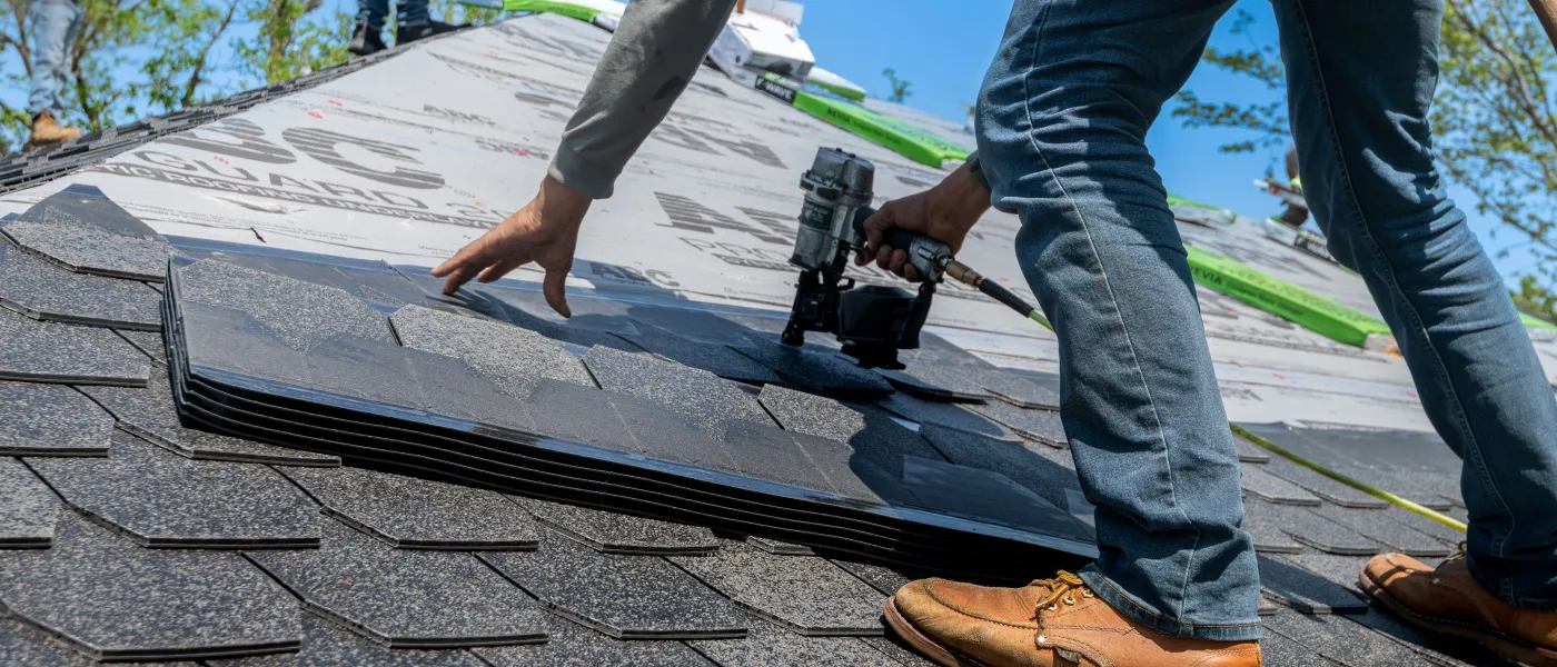 Roofer using a nail gun to install shingles on a new roof